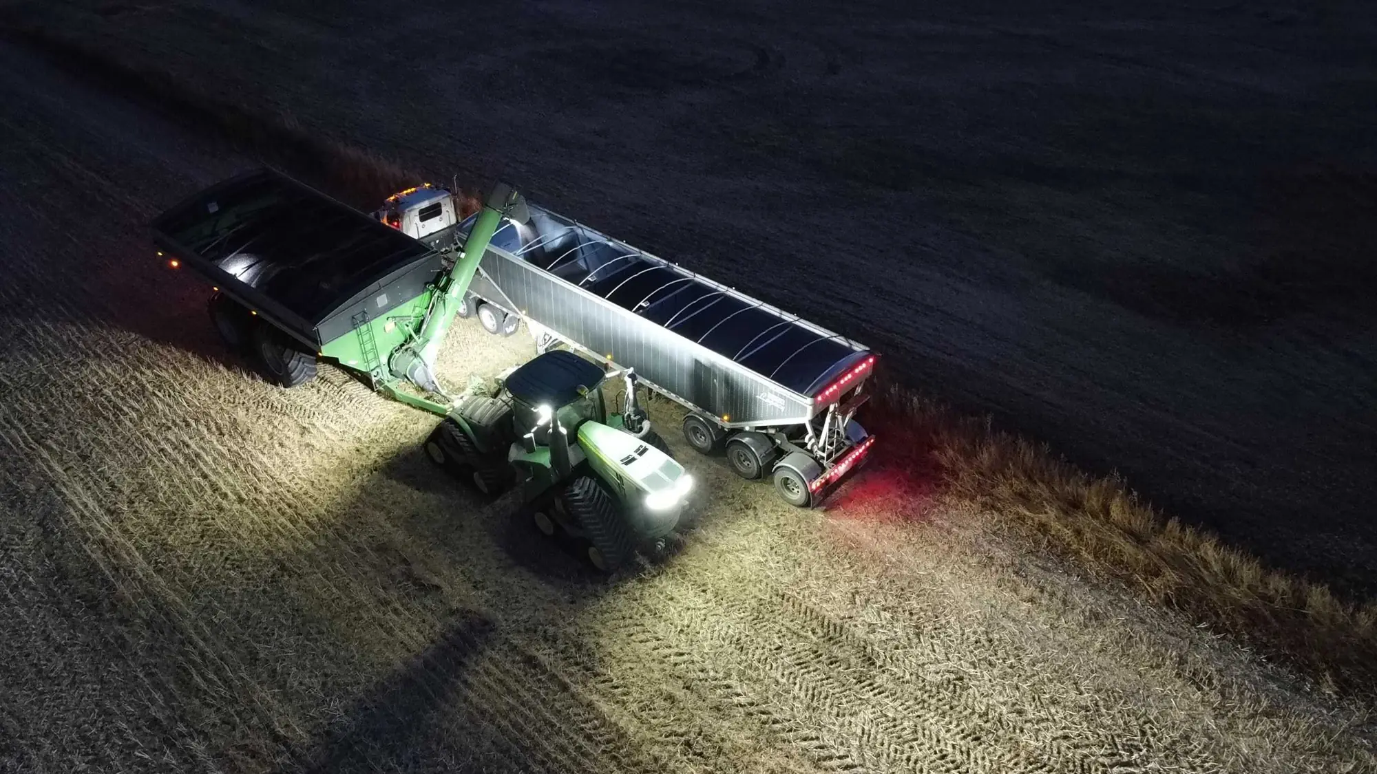 A grain cart unloading into a truck at night in a Saskatchewan field.